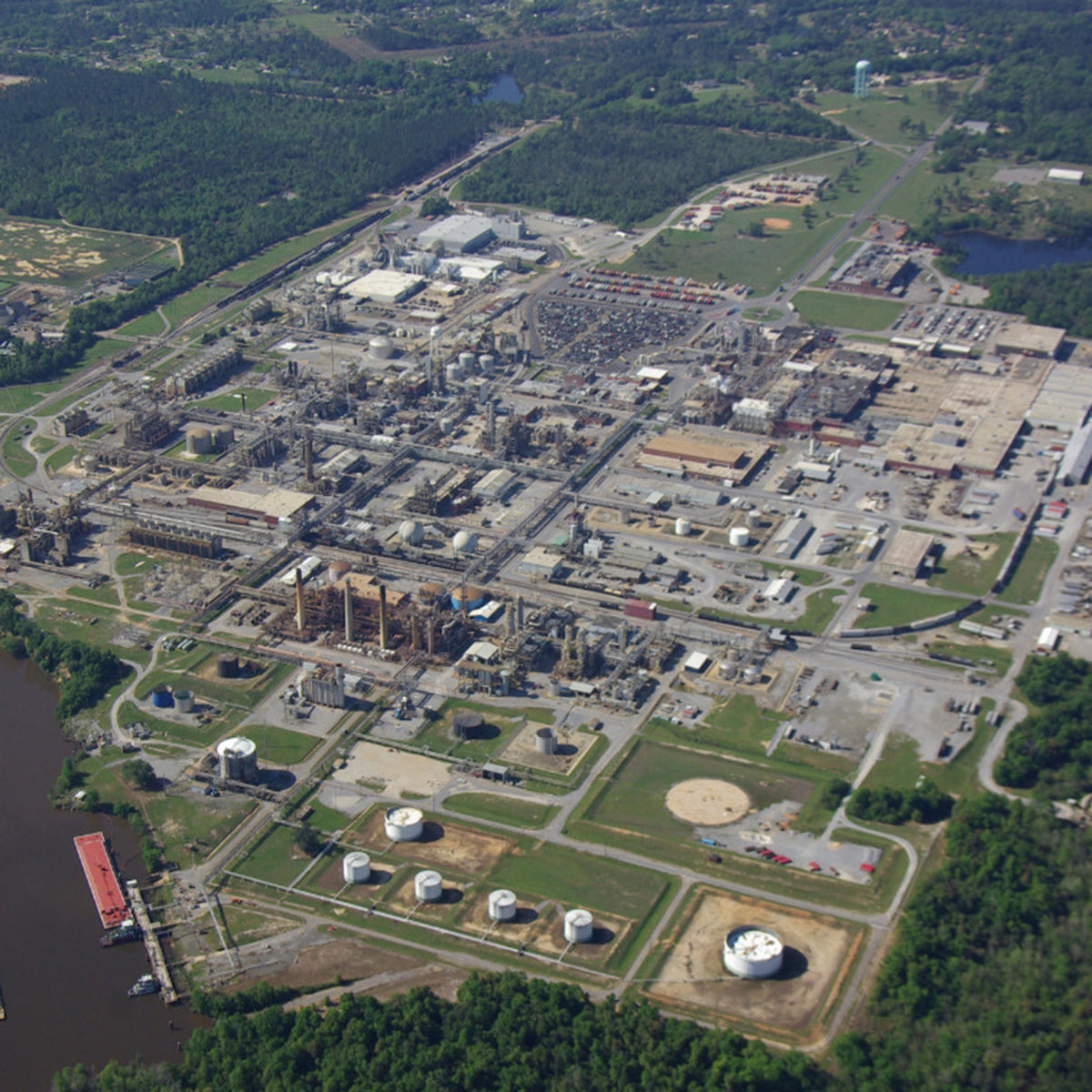 Areal image of a factory area located in an area with wood and a lake.