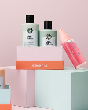 Maria Nila True Soft shampoo and conditioner bottles with a pink spray bottle on a pastel background